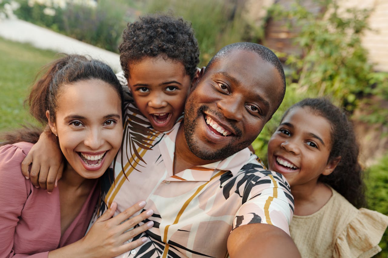 A joyful black family taking a selfie outdoors in a lush garden setting.