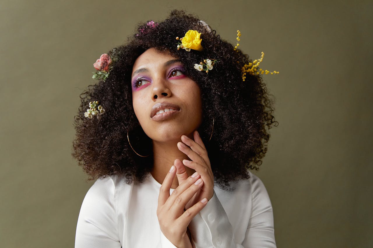 Close-up portrait of a woman with afro hair adorned with flowers, showcasing vibrant makeup.