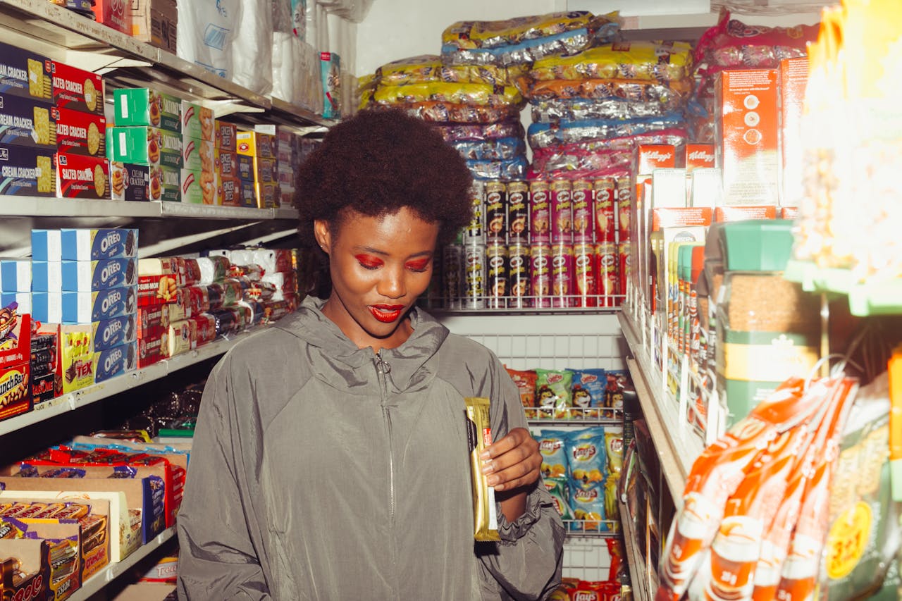 A smiling woman examines products in a colorful grocery store aisle.