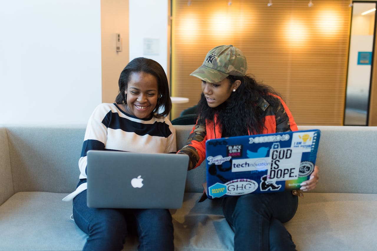 Two women pair programming on laptops, sharing ideas and working together indoors.