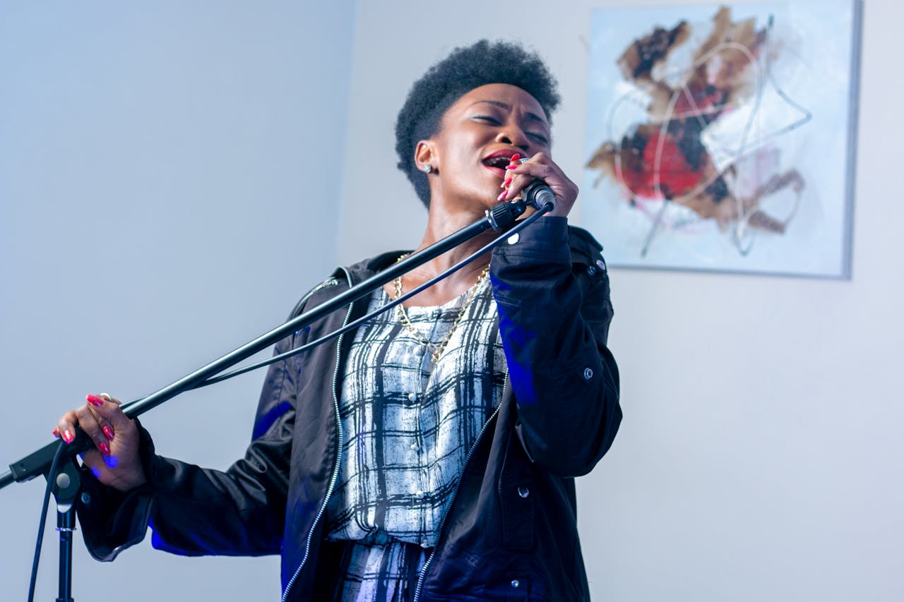 African American woman singing passionately into a microphone indoors.